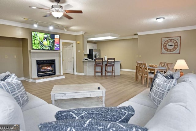 living room featuring hardwood / wood-style flooring, ceiling fan, ornamental molding, and a textured ceiling