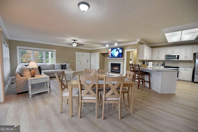 dining room featuring ceiling fan, light hardwood / wood-style floors, ornamental molding, and a textured ceiling
