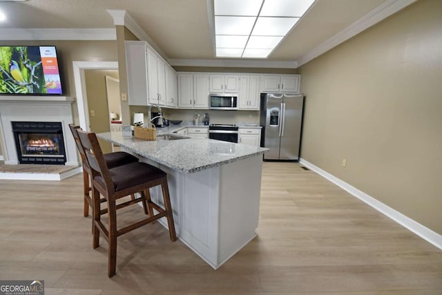 kitchen featuring sink, a breakfast bar area, light stone countertops, white cabinetry, and stainless steel appliances