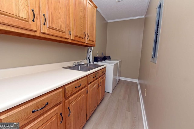washroom featuring washing machine and clothes dryer, sink, cabinets, crown molding, and light wood-type flooring
