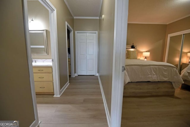corridor with a textured ceiling, sink, crown molding, and light hardwood / wood-style flooring