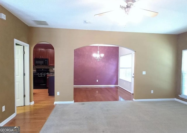 empty room with plenty of natural light, wood-type flooring, and ceiling fan with notable chandelier