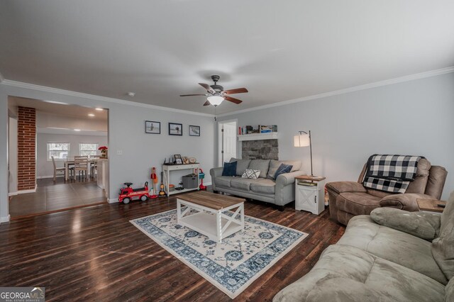 living room featuring crown molding, ceiling fan, dark wood-type flooring, and a stone fireplace