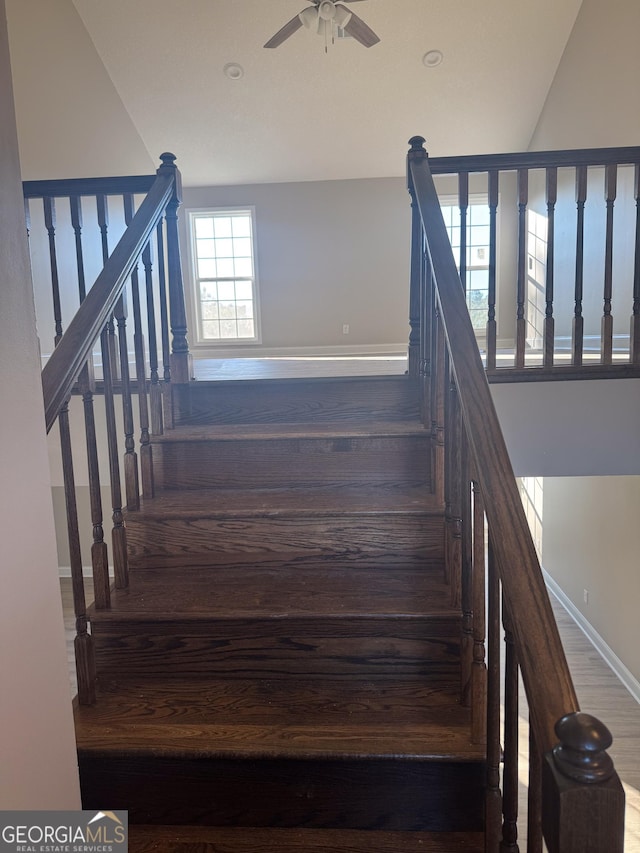 staircase with ceiling fan, hardwood / wood-style floors, and vaulted ceiling