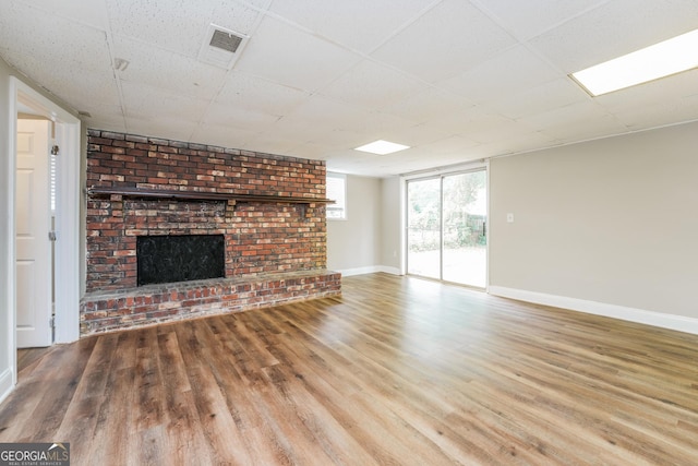 unfurnished living room featuring wood-type flooring, a brick fireplace, and a drop ceiling