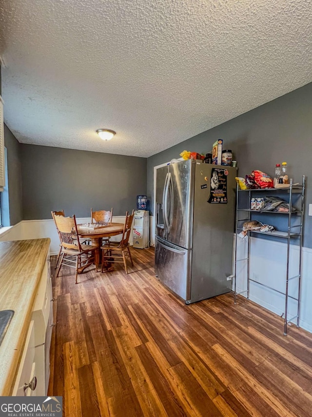 kitchen with stainless steel fridge, dark wood-type flooring, and a textured ceiling