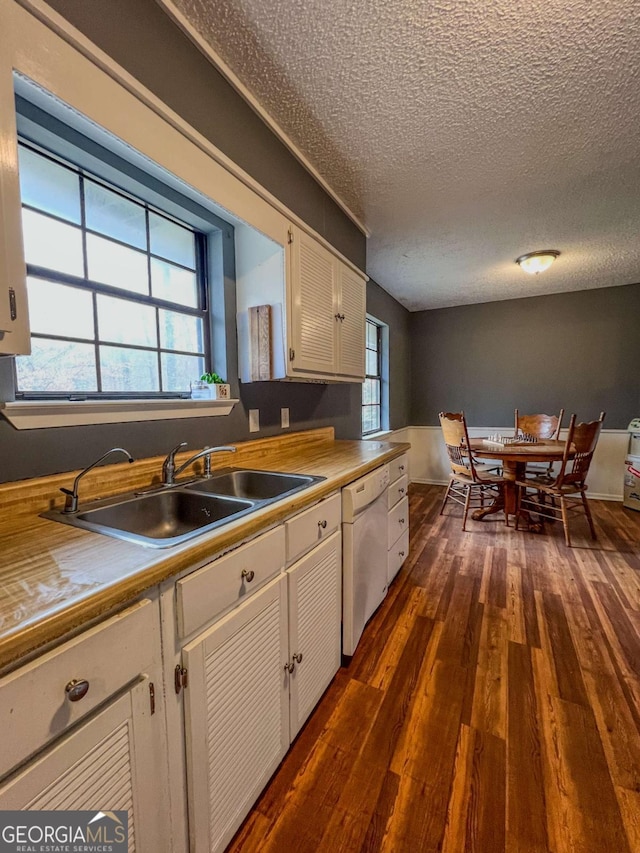 kitchen featuring white dishwasher, sink, white cabinetry, and dark wood-type flooring