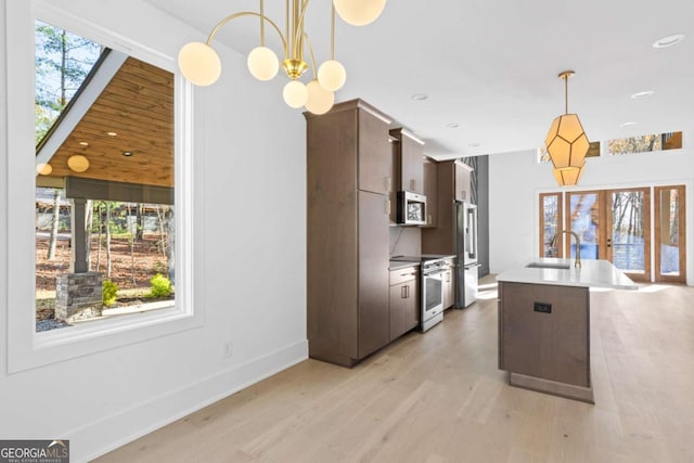 kitchen featuring light hardwood / wood-style floors, appliances with stainless steel finishes, hanging light fixtures, dark brown cabinetry, and sink