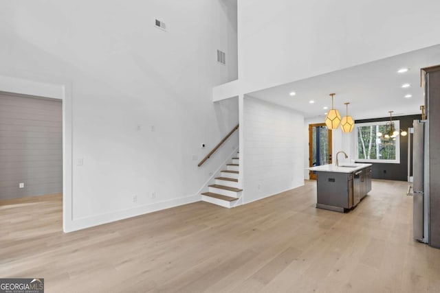 kitchen featuring decorative light fixtures, sink, light wood-type flooring, an island with sink, and a chandelier