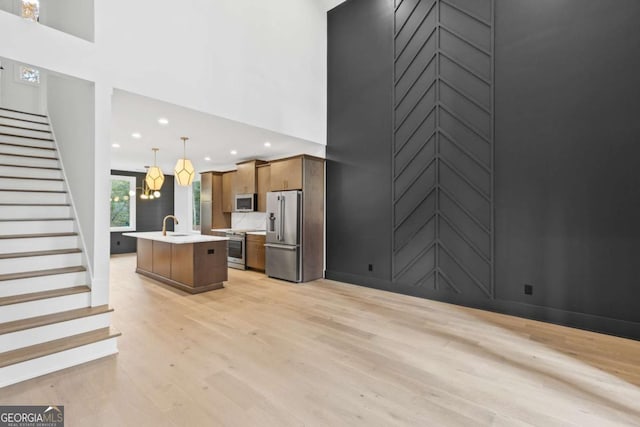 kitchen with pendant lighting, stainless steel appliances, sink, a kitchen island with sink, and light hardwood / wood-style flooring