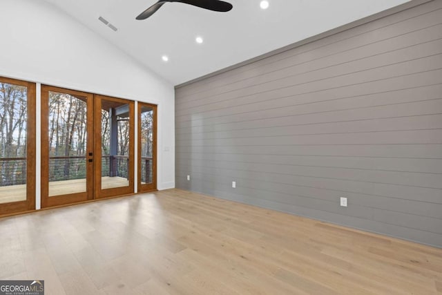 spare room featuring french doors, high vaulted ceiling, wood walls, ceiling fan, and light hardwood / wood-style flooring