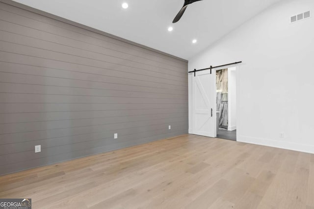 unfurnished bedroom with ceiling fan, light wood-type flooring, a barn door, and vaulted ceiling