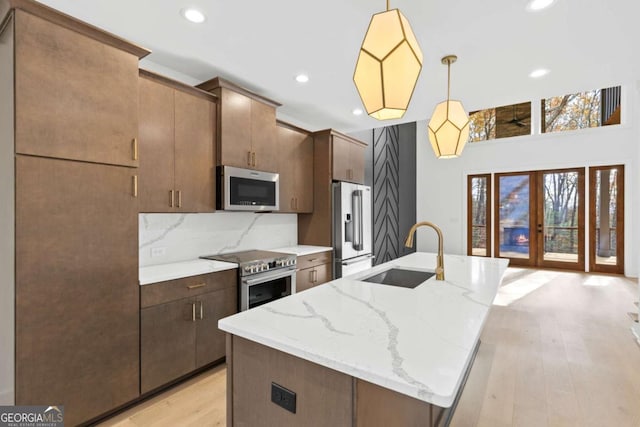 kitchen featuring appliances with stainless steel finishes, a kitchen island with sink, decorative light fixtures, light stone counters, and sink