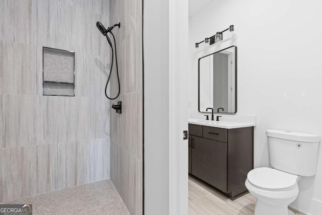 bathroom featuring toilet, a tile shower, and vanity