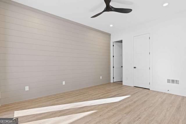 unfurnished bedroom featuring ceiling fan, light hardwood / wood-style floors, and wood walls