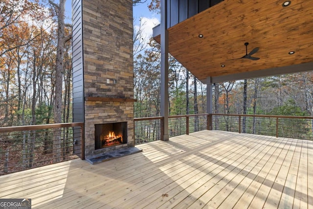 wooden terrace with ceiling fan and an outdoor stone fireplace