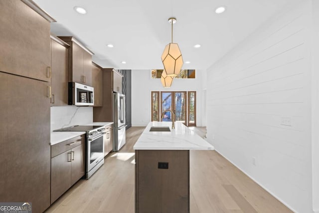 kitchen with light stone countertops, pendant lighting, stainless steel appliances, sink, and a kitchen island with sink