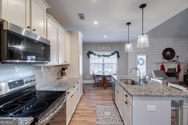 kitchen featuring sink, appliances with stainless steel finishes, an island with sink, light stone countertops, and white cabinets