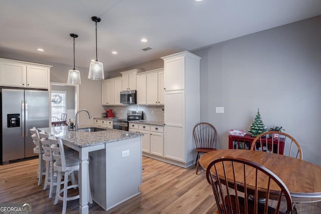 kitchen featuring white cabinetry, sink, stainless steel appliances, light stone countertops, and a center island with sink