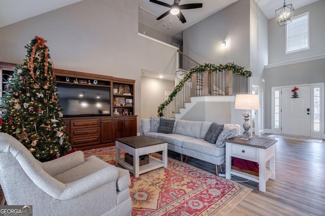 living room featuring a towering ceiling, wood-type flooring, a healthy amount of sunlight, and ceiling fan with notable chandelier