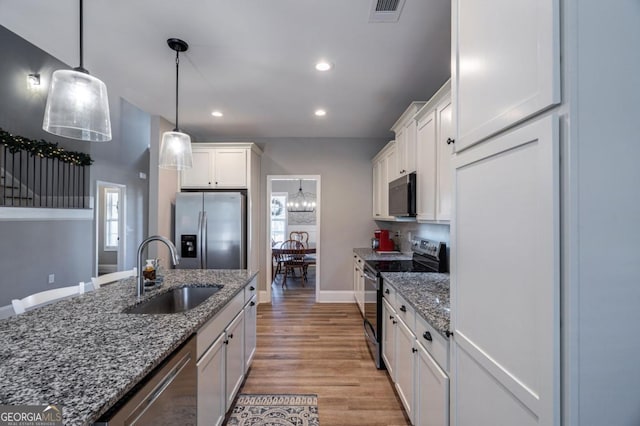 kitchen with sink, decorative light fixtures, dark stone counters, stainless steel appliances, and white cabinets