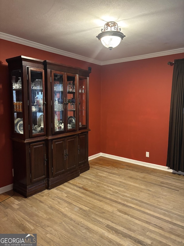 spare room with light wood-type flooring, a textured ceiling, baseboards, and crown molding