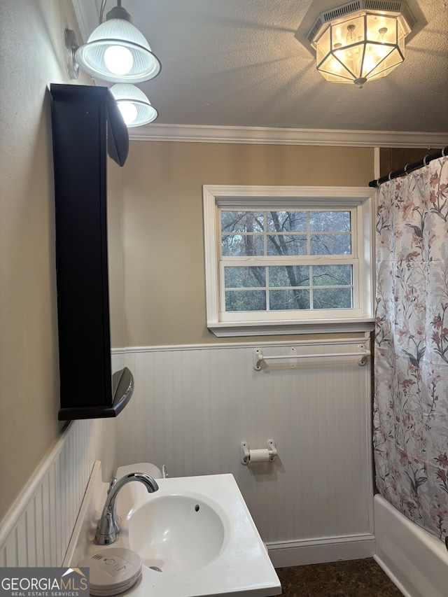 bathroom with shower / bath combo, a wainscoted wall, ornamental molding, a textured ceiling, and a sink