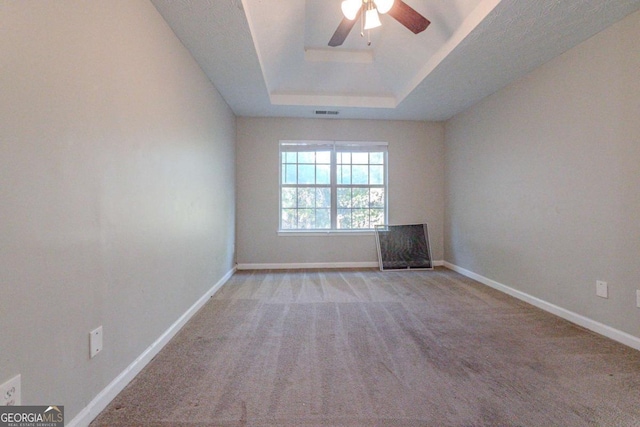 empty room featuring ceiling fan, a raised ceiling, and light carpet