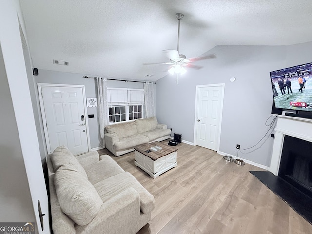 living room with a textured ceiling, ceiling fan, lofted ceiling, and light wood-type flooring