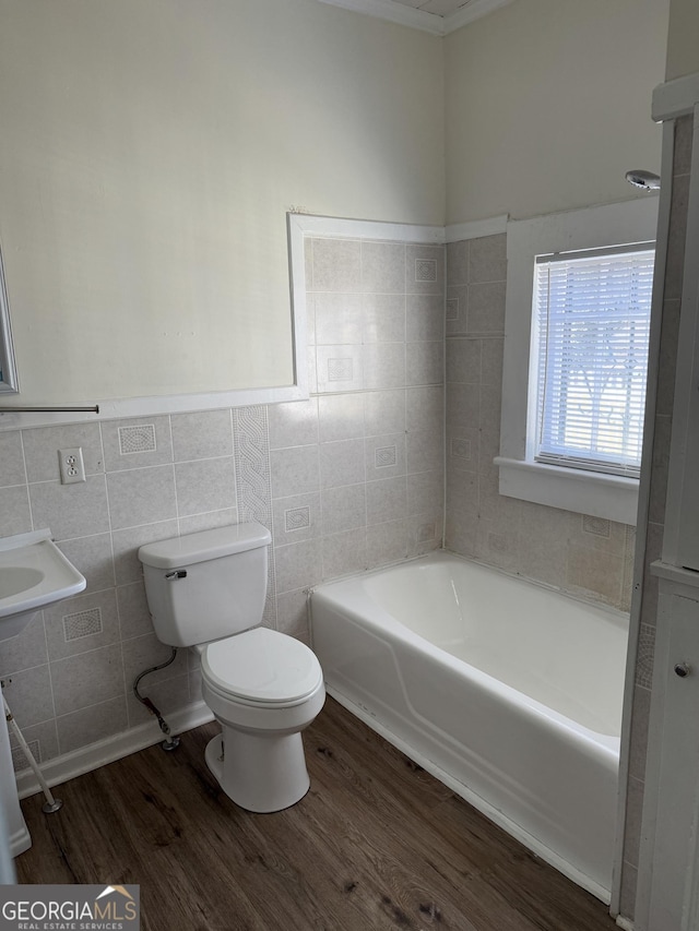 bathroom featuring a washtub, wood-type flooring, toilet, and tile walls