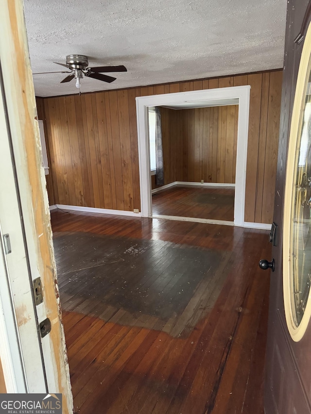 foyer featuring a textured ceiling, dark hardwood / wood-style flooring, ceiling fan, and wooden walls