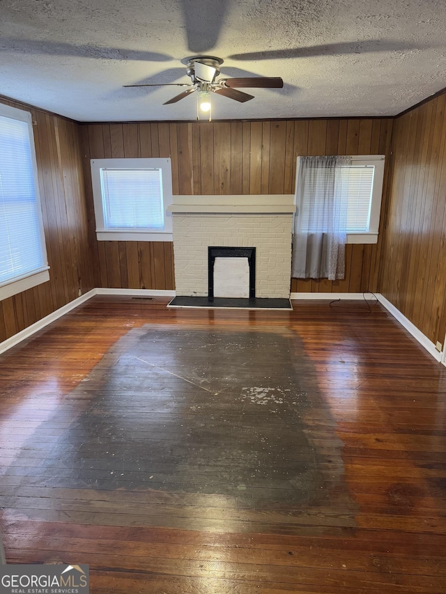 unfurnished living room with dark hardwood / wood-style floors, a healthy amount of sunlight, a textured ceiling, and a brick fireplace