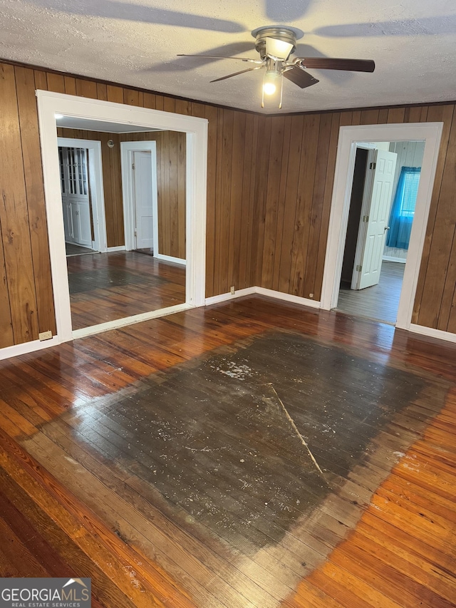 spare room with a textured ceiling, ceiling fan, wood walls, and dark wood-type flooring