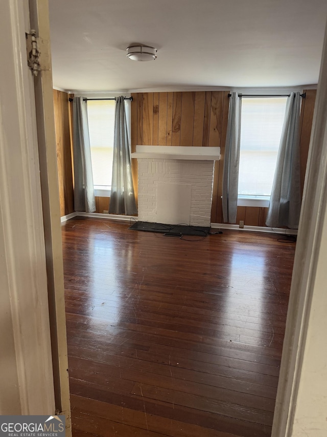 empty room with dark hardwood / wood-style flooring, a brick fireplace, and plenty of natural light