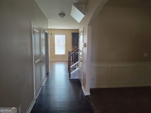 corridor with dark wood-type flooring and an inviting chandelier