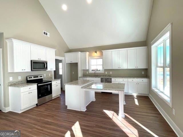 kitchen with appliances with stainless steel finishes, high vaulted ceiling, a kitchen island, and white cabinetry