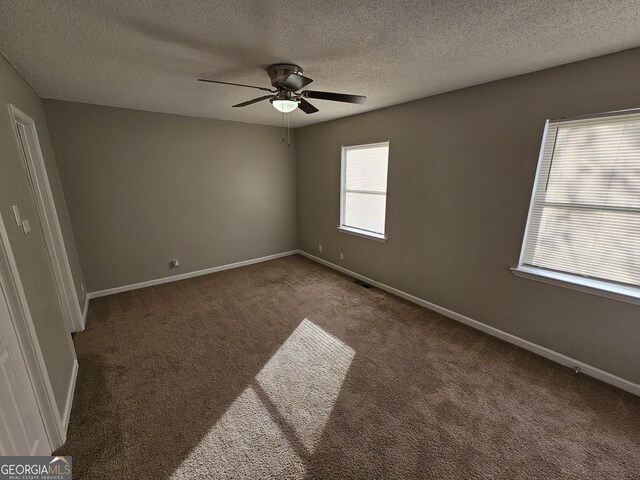 spare room featuring ceiling fan, dark carpet, and a textured ceiling