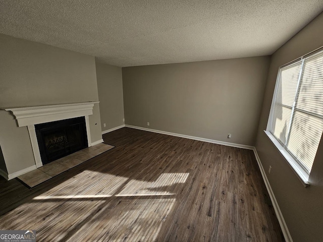 unfurnished living room with baseboards, a fireplace with flush hearth, a textured ceiling, and wood finished floors