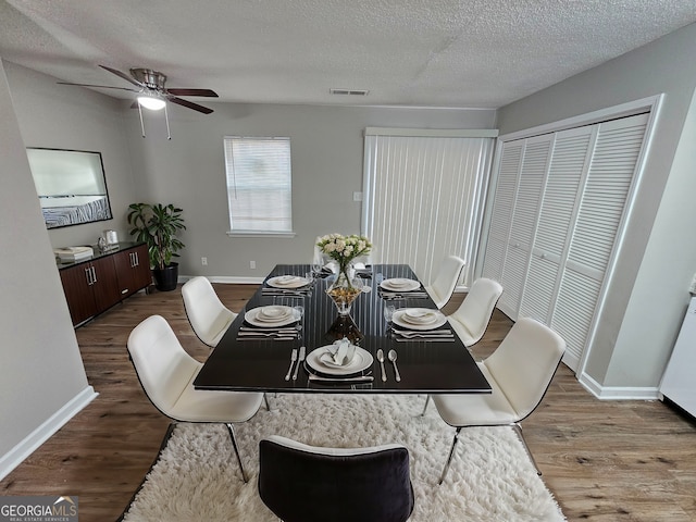 dining space with a ceiling fan, baseboards, wood finished floors, visible vents, and a textured ceiling