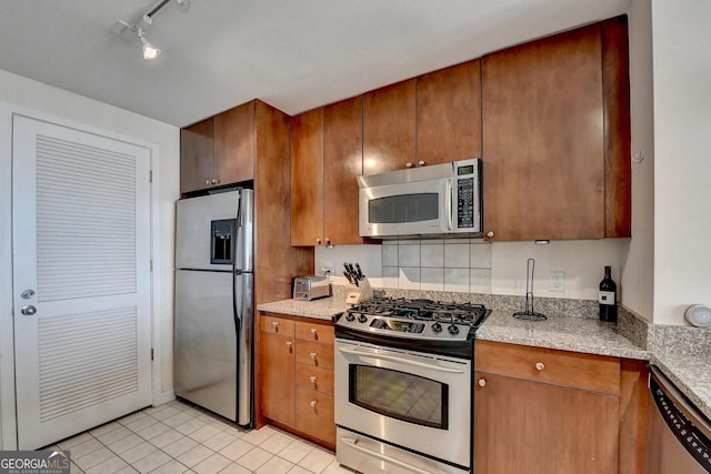 kitchen with light stone counters, light tile patterned flooring, stainless steel appliances, and track lighting