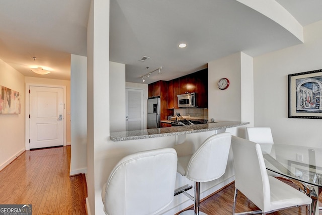 kitchen with kitchen peninsula, appliances with stainless steel finishes, backsplash, light stone counters, and a breakfast bar