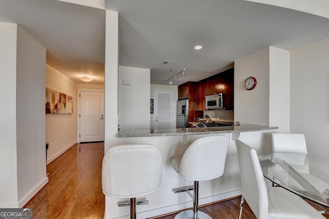 kitchen with light stone countertops, stainless steel appliances, kitchen peninsula, a kitchen bar, and decorative backsplash