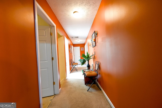 hallway with light colored carpet and a textured ceiling