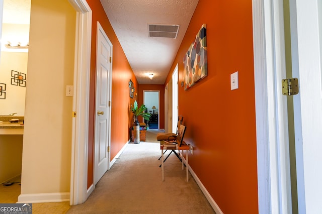 hallway featuring light colored carpet and a textured ceiling