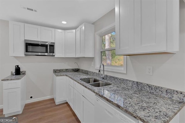 kitchen featuring light stone countertops, light wood-type flooring, sink, dishwasher, and white cabinetry