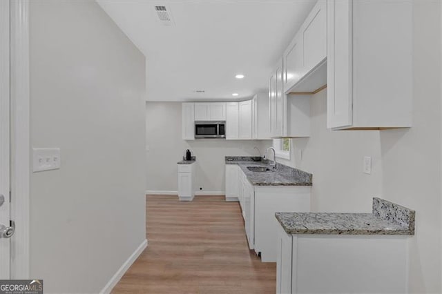 kitchen featuring light stone countertops, sink, white cabinets, and light hardwood / wood-style floors