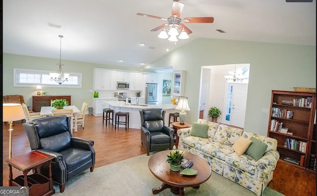 living room with ceiling fan with notable chandelier, light wood-type flooring, lofted ceiling, and sink