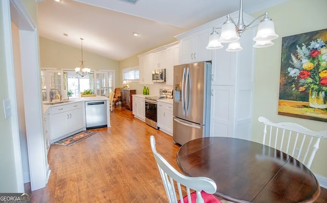 kitchen featuring appliances with stainless steel finishes, light wood-type flooring, decorative light fixtures, white cabinets, and lofted ceiling