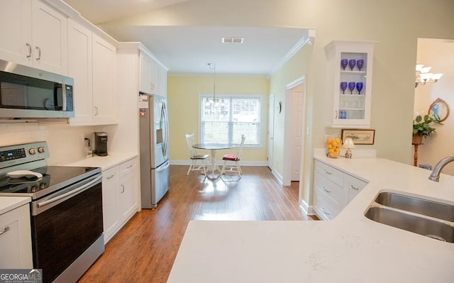 kitchen featuring white cabinetry, sink, hanging light fixtures, light hardwood / wood-style flooring, and appliances with stainless steel finishes