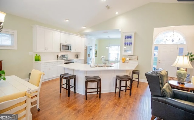 kitchen with a kitchen bar, appliances with stainless steel finishes, white cabinets, light hardwood / wood-style floors, and lofted ceiling